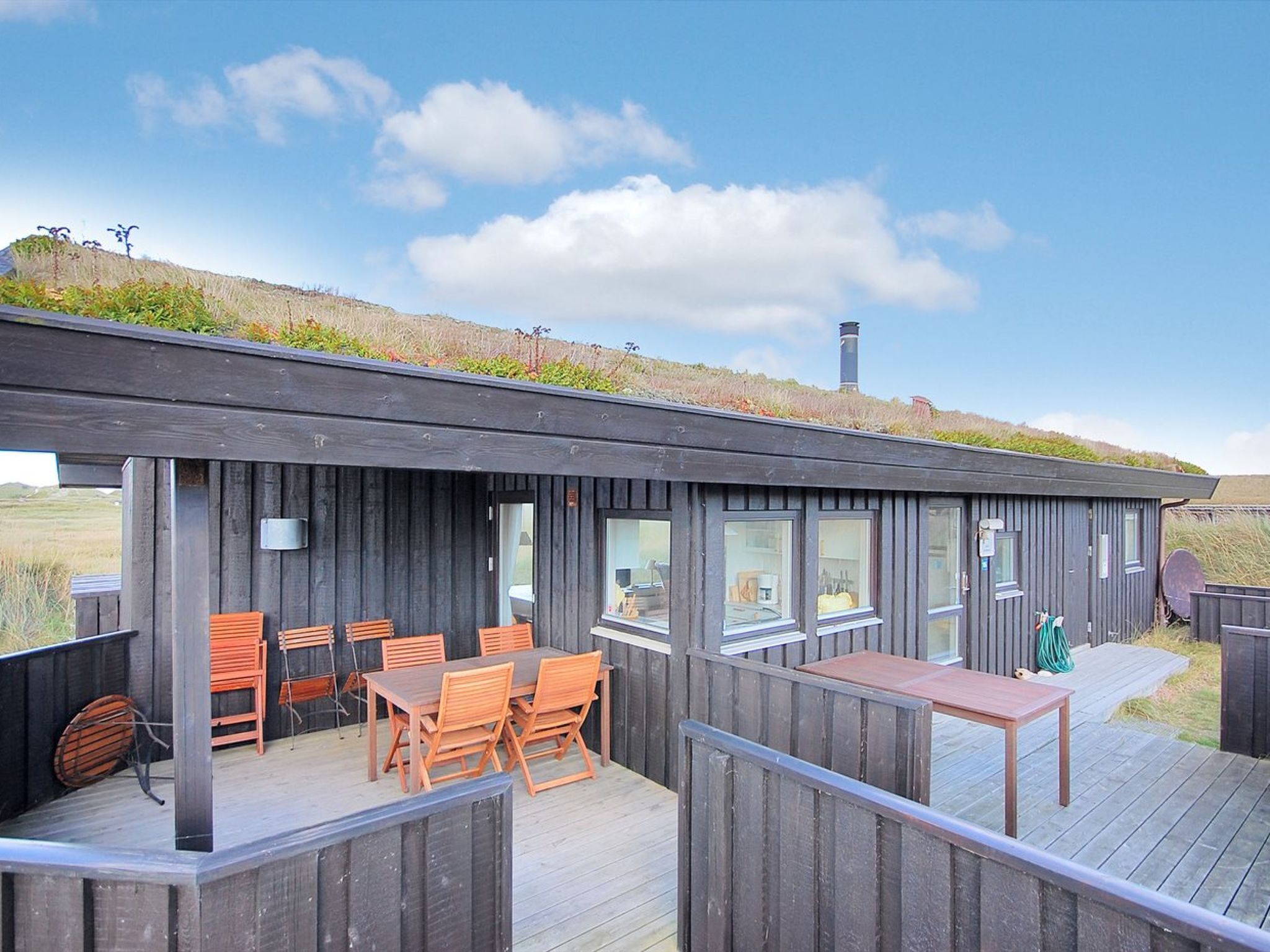 A modern wooden building with a flat roof, large windows, and a deck area with outdoor furniture.