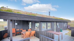 Un bâtiment moderne en bois, doté d’un toit plat, de grandes fenêtres et d’une terrasse aménagée avec du mobilier d’extérieur.