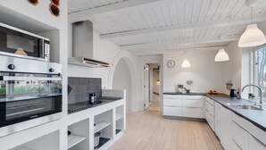 Une cuisine moderne avec des meubles blancs, un four encastré et des luminaires suspendus.