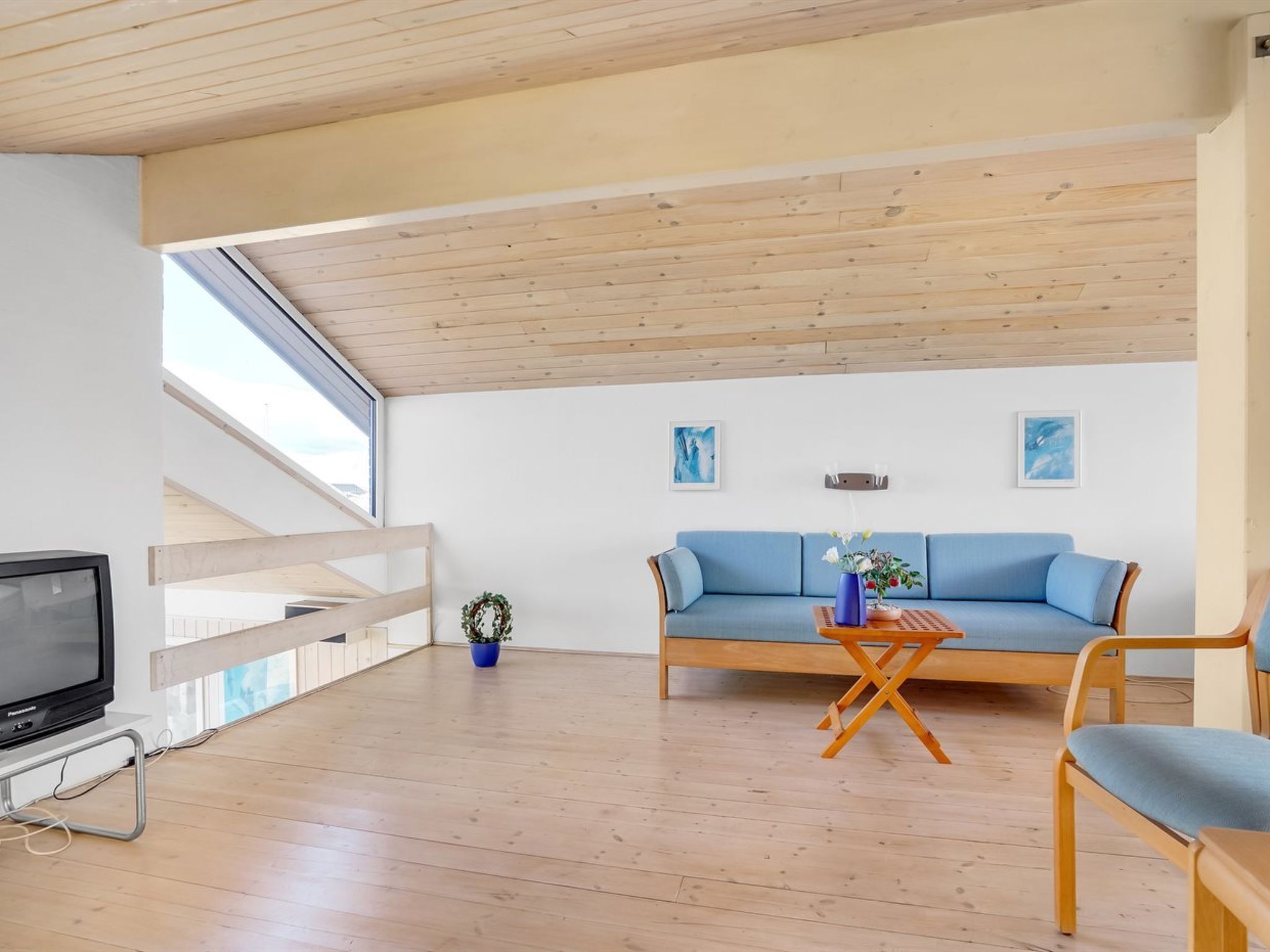 Una sala de estar moderna con techo de madera, un sofá azul, un televisor y una escalera.