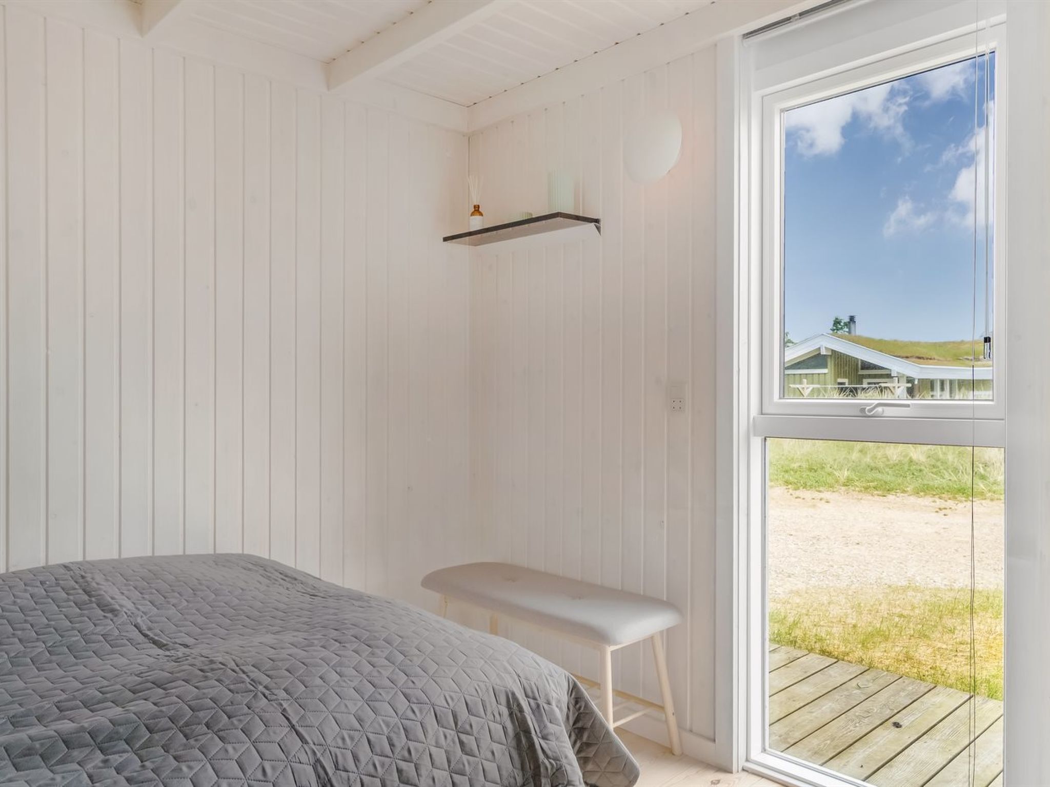 Ein Zimmer mit einem Bett, einer Sitzbank, einem Fenster und einem Regal.