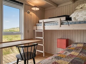 Un lit superposé avec un bureau et une chaise, une fenêtre donnant sur une pelouse et un placard rouge.