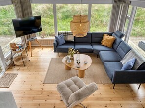 A modern living room with a sectional sofa, a round coffee table, a TV, and a wicker lamp.