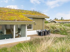Une maison moderne avec un toit recouvert d’herbe, une terrasse dotée de mobilier d’extérieur et une vue sur le paysage environnant.