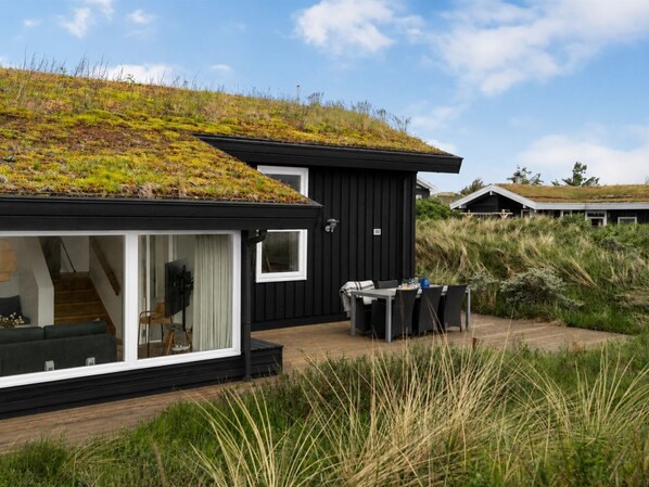 A modern house with a green roof, a glass door entrance, and a patio with outdoor furniture.