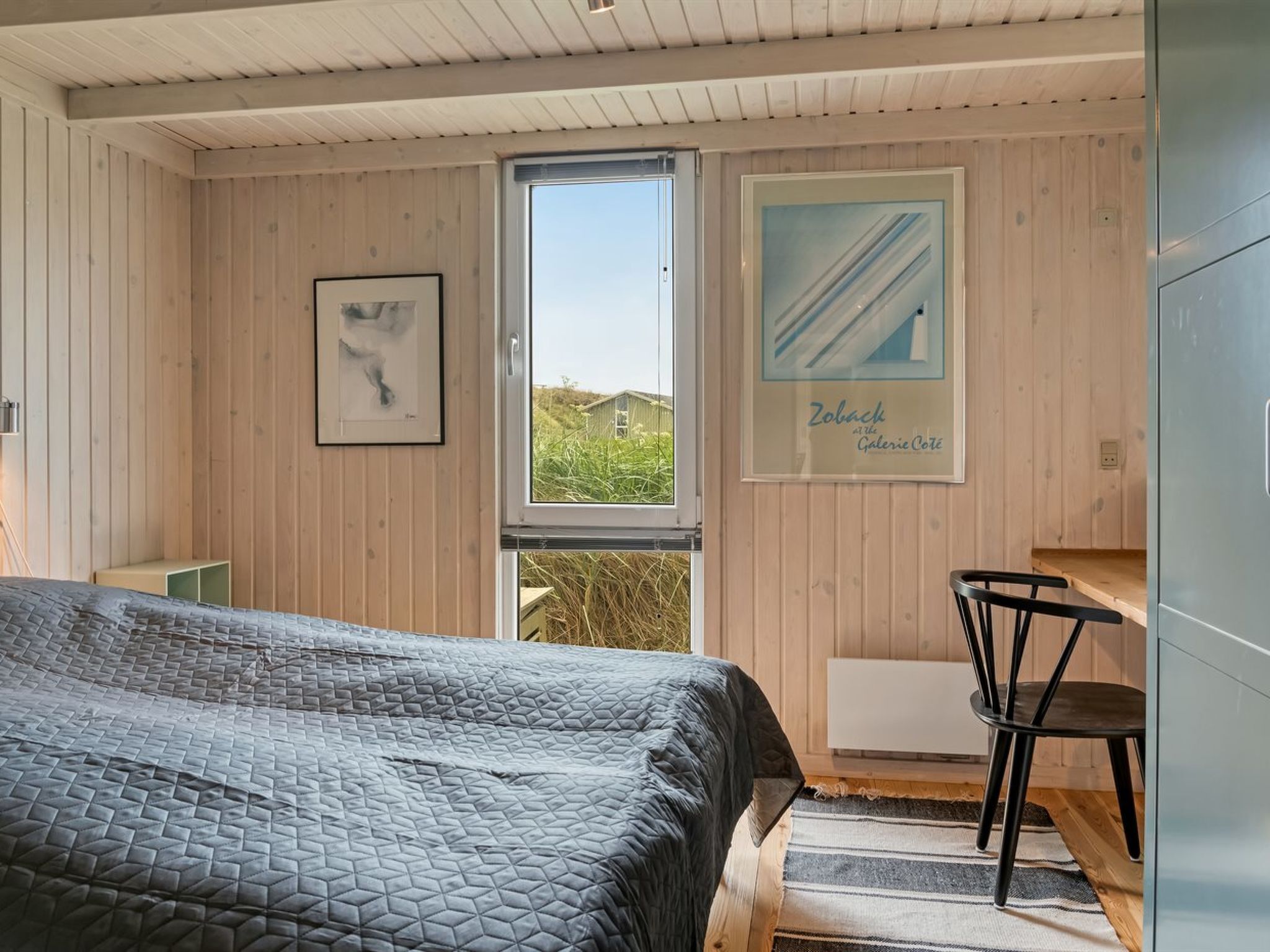 A bedroom with a bed, a window, a chair, and a poster on the wall.