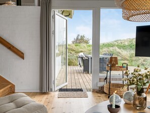 A modern interior with a wooden staircase, a sliding glass door leading to an outdoor deck, and a flat-screen TV mounted on the wall.