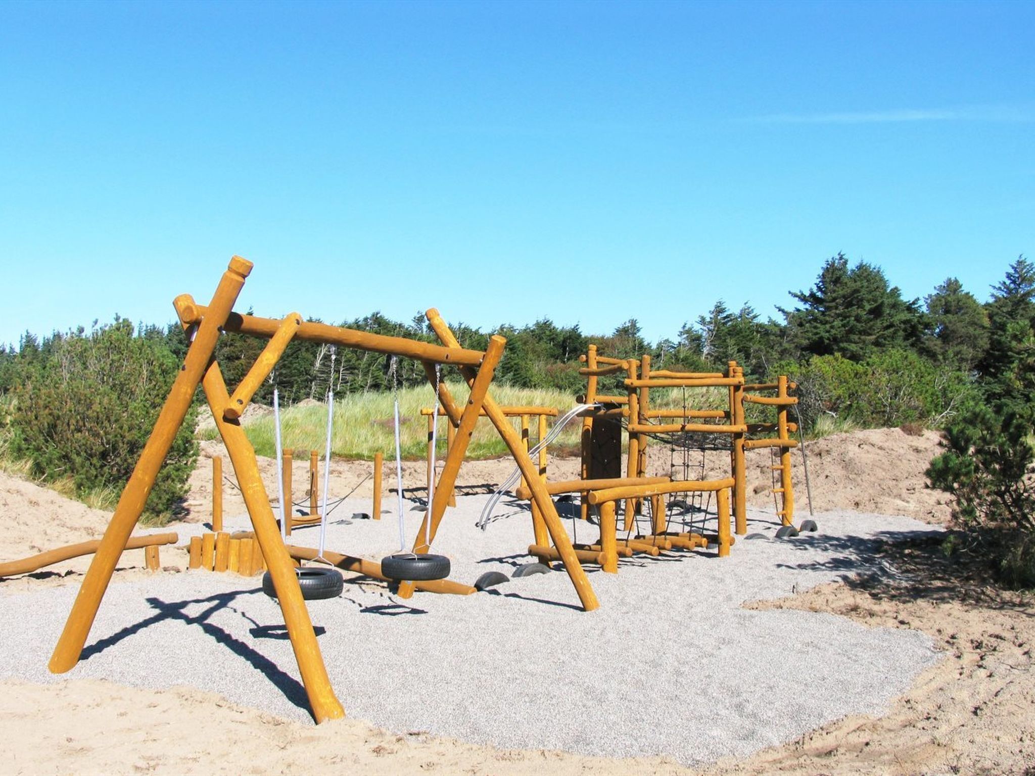 A playground with wooden structures and tires on a sandy area.