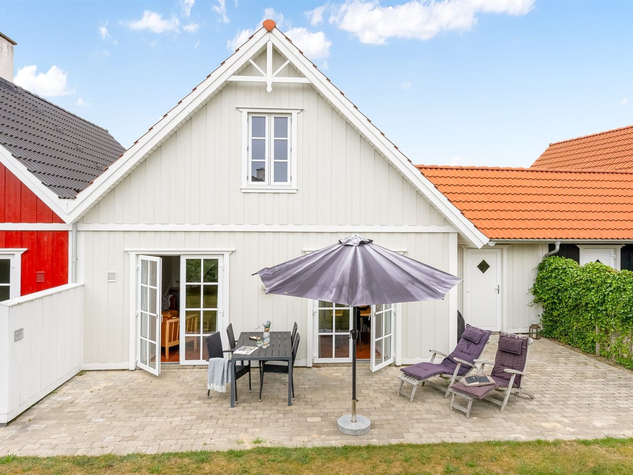 A white building with a gabled roof, a patio with a table and chairs, and a covered seating area.