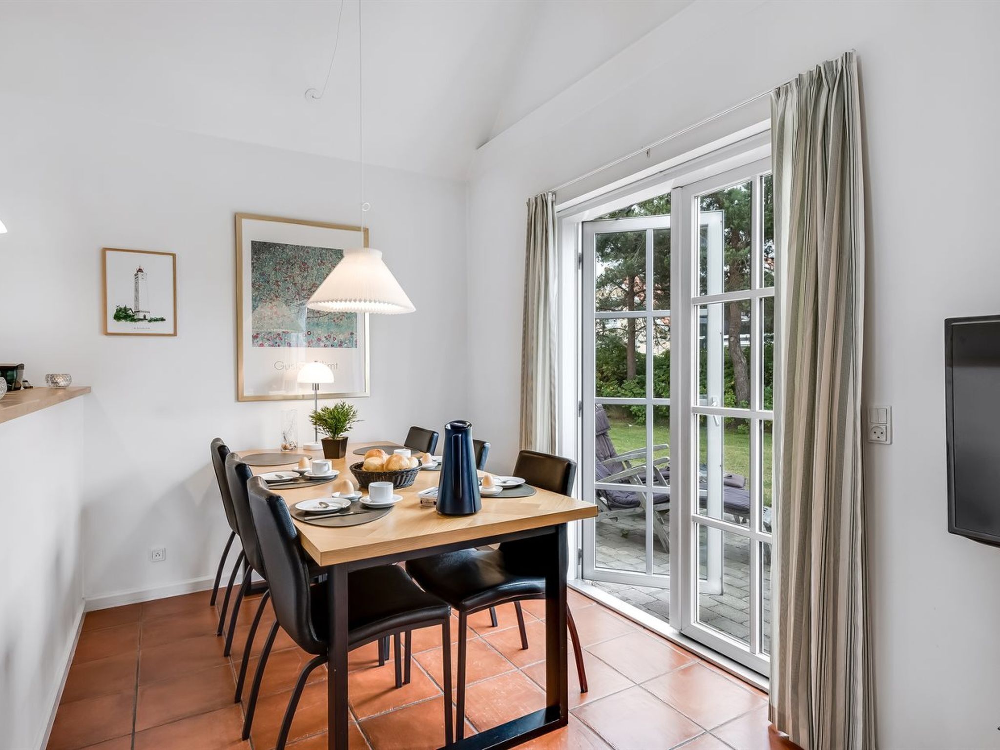 Un coin repas avec une table dressée pour quatre personnes, une lampe et une vue sur l’extérieur grâce à une grande fenêtre.