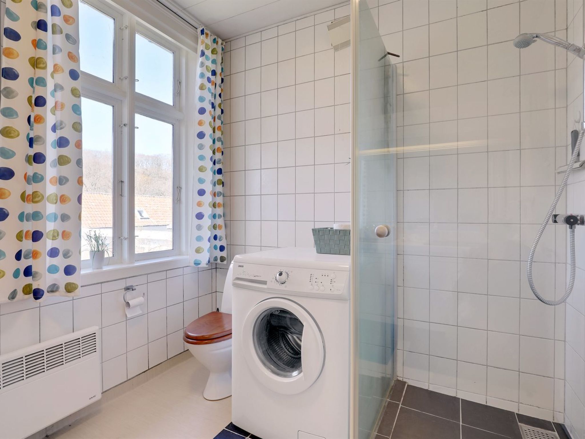 A bathroom with a washing machine, toilet, and shower.