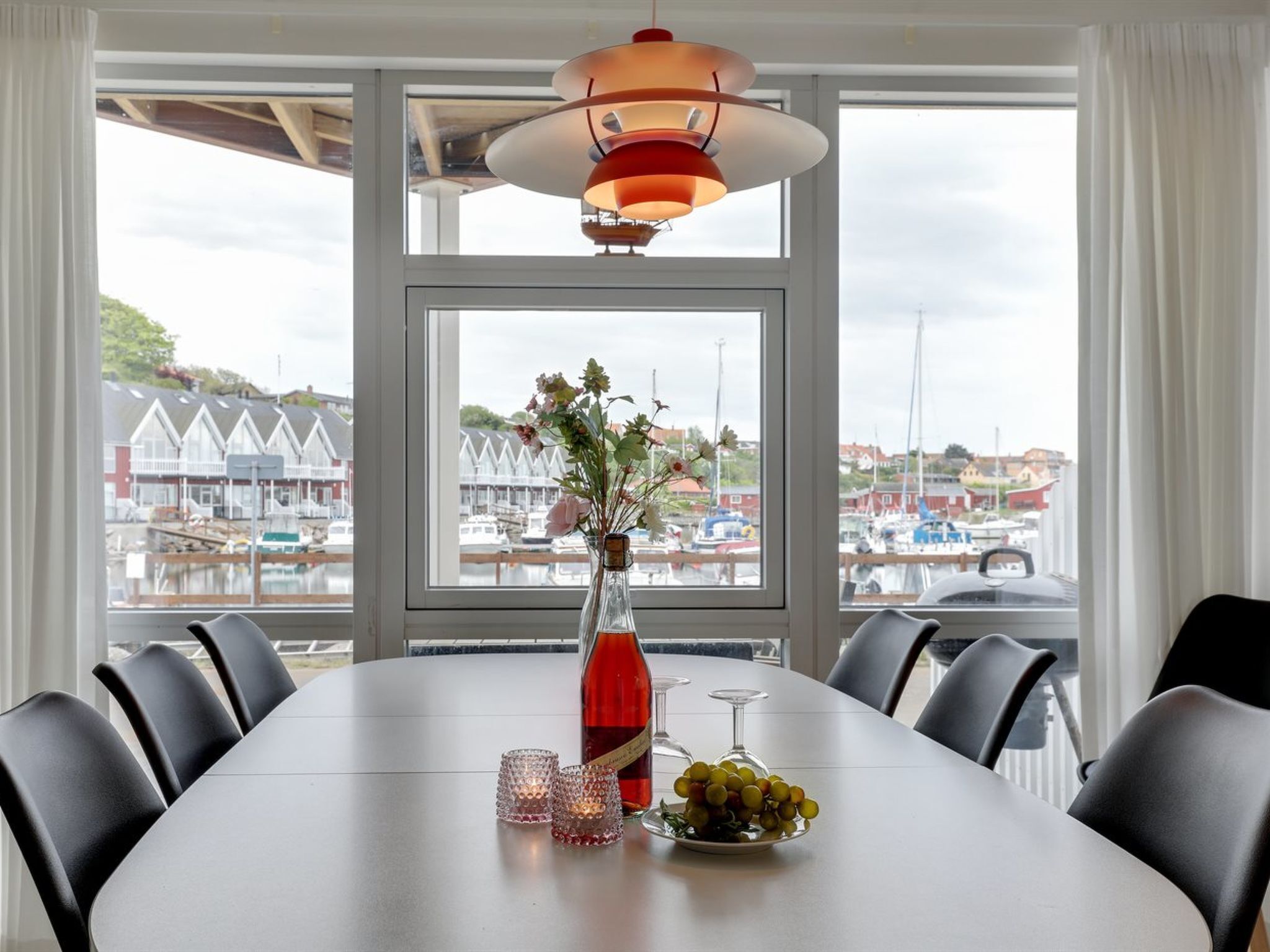 A dining table with chairs, a vase with flowers, a bottle, and a bowl of grapes.