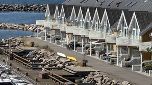 Fileira de edifícios brancos em estilo chalé, com telhado inclinado, localizada junto a uma costa rochosa e vista para o mar.