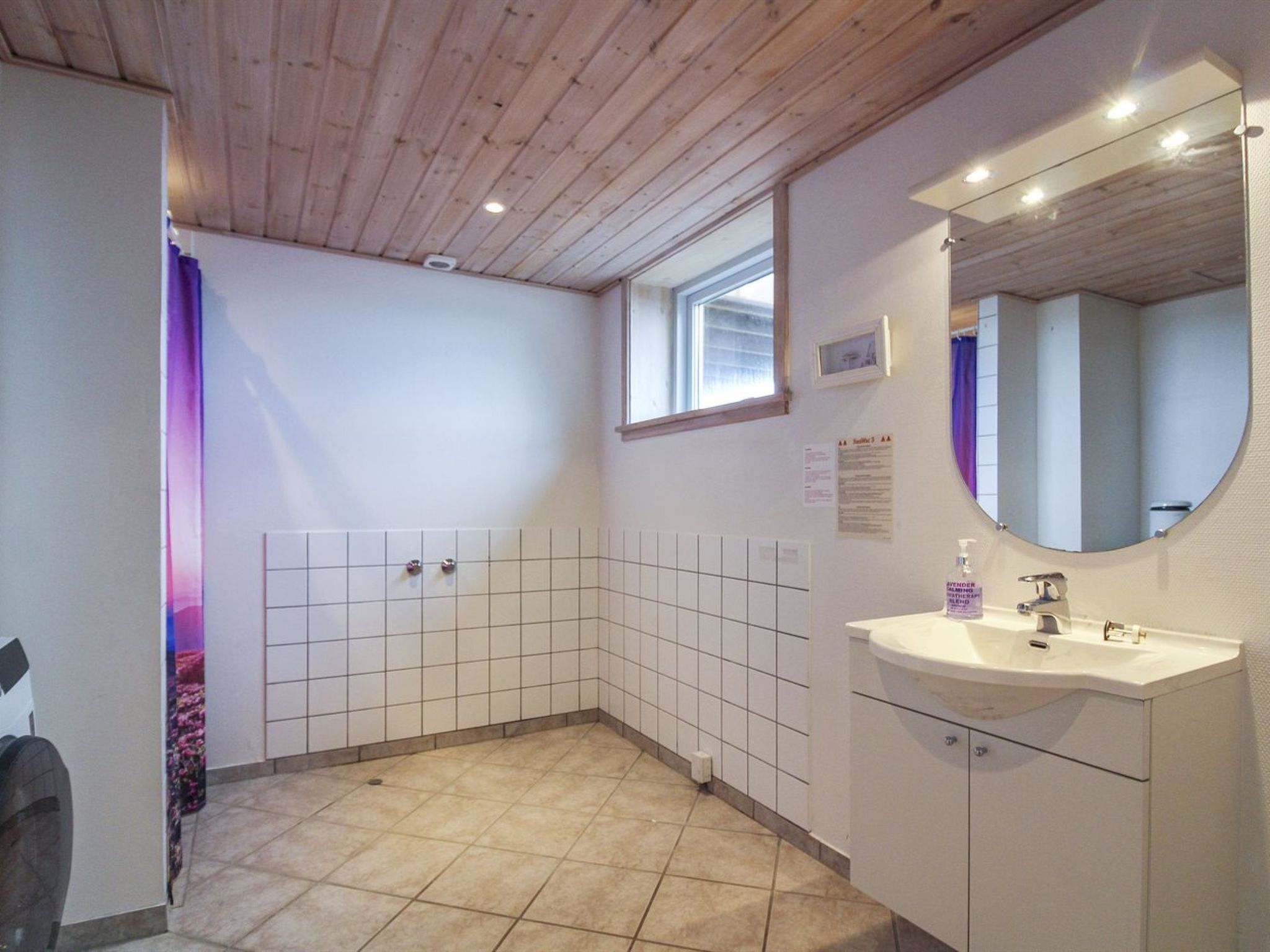 Une salle de bain avec un plafond en bois, une fenêtre, un sol carrelé, un lavabo et un miroir.
