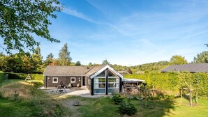 Ein modernes Haus mit großem Glasanbau, einem Holzschuppen und einem Weinberg im Hintergrund.