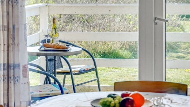 Un comedor con una mesa redonda, sillas, una mesita con una botella y vasos, y vistas al exterior con zonas verdes.