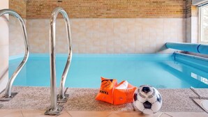 Una piscina con escaleras de metal, un banco azul y un balón de fútbol en el suelo.