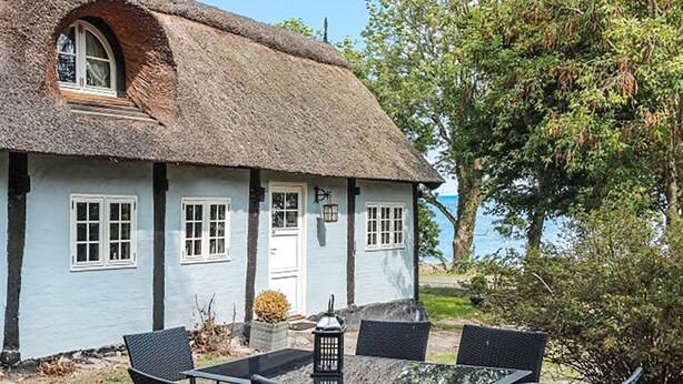 A thatched-roof cottage with a small porch and a table with chairs in front.
