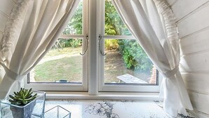 A room with a large window featuring white curtains, a potted plant, and a floral design on the window frame.