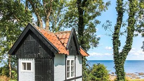 A small, two-story house with a black and white exterior, a red roof, and a view of the sea.
