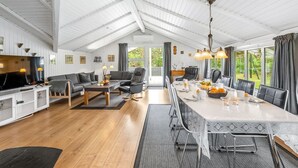 Un vaste espace de vie avec un plafond haut, une table à manger pour quatre personnes et un téléviseur placé dans un coin.
