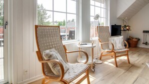 A room with two wooden chairs with mesh backs, a small round table, a TV on a stand, and large windows offering a view of the outside. - "Joona" - 12km from the sea by Interhome (Oksbøl)
