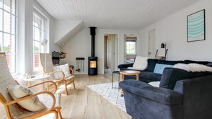 A spacious living room with a high ceiling, a black wood-burning stove, a dark blue sofa, and a wooden chair with cushions. - "Joona" - 12km from the sea by Interhome (Oksbøl)