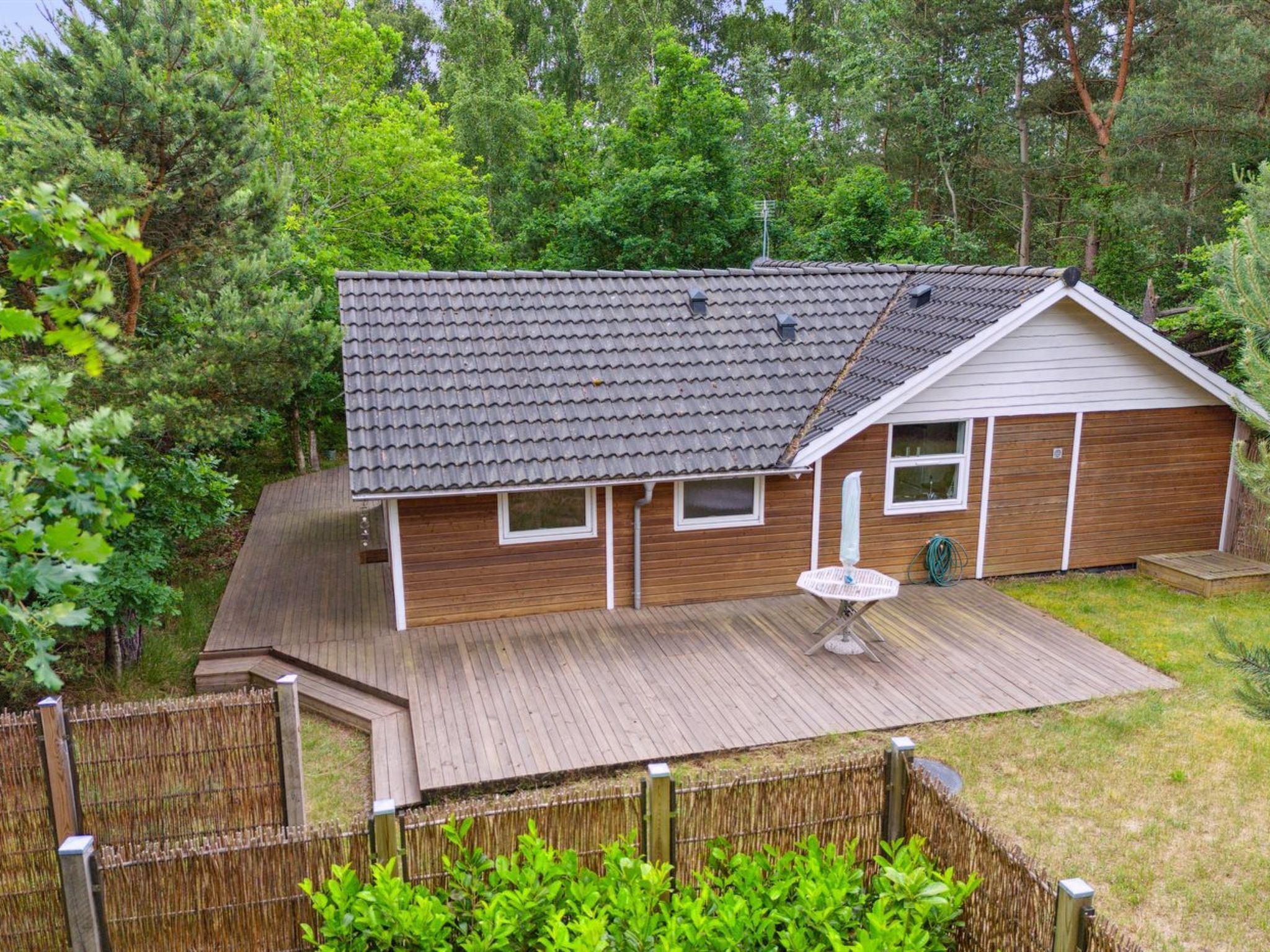 A single-story house with a tiled roof, wooden siding, and a fenced backyard.