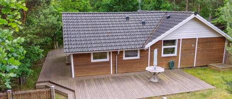 A single-story house with a tiled roof, wooden siding, and a fenced backyard.