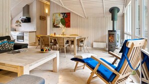 En hyggelig indretning med spiseplads, sofa, lænestol og brændeovn.