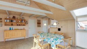 Un intérieur chaleureux en bois, avec un coin repas comprenant une table et des chaises, une bibliothèque et un coin cuisine équipé d’un four à micro-ondes.
