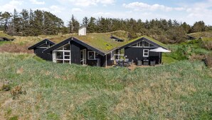 Une maison moderne dotée d’un toit végétalisé, située dans un espace verdoyant, avec des arbres en arrière-plan.