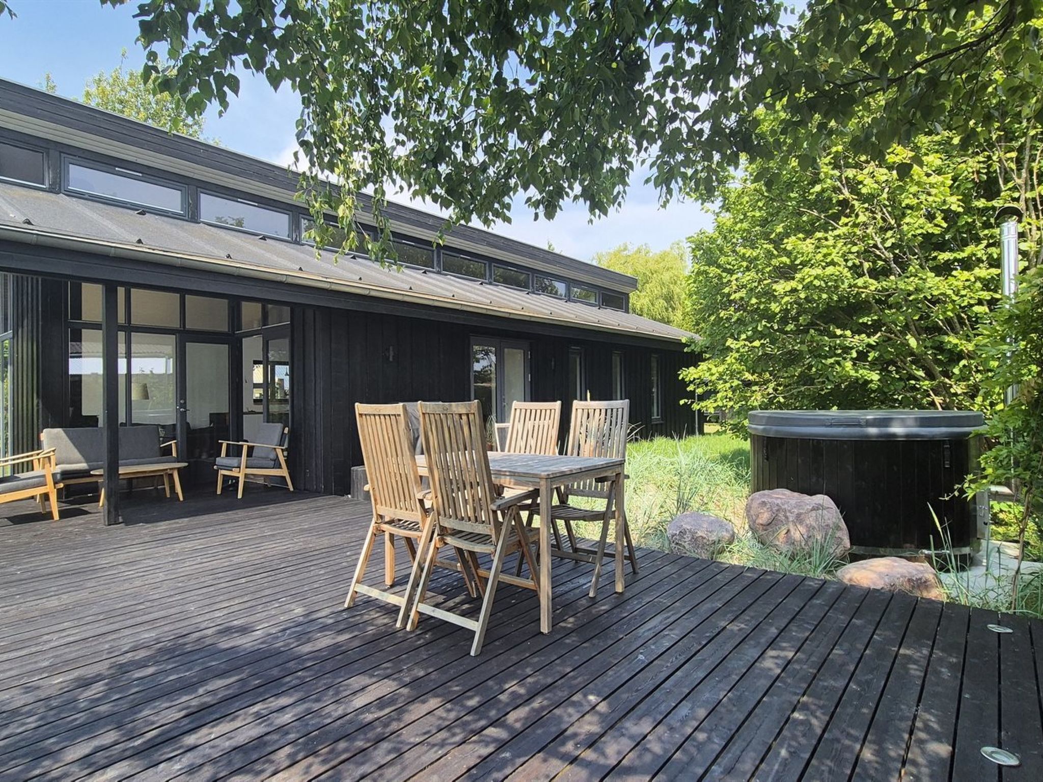 A modern outdoor deck with wooden furniture, a hot tub, and a view of a building with large windows.