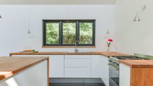 Een moderne keuken met een groot raam, witte kastjes, een houten aanrecht en een gasfornuis.