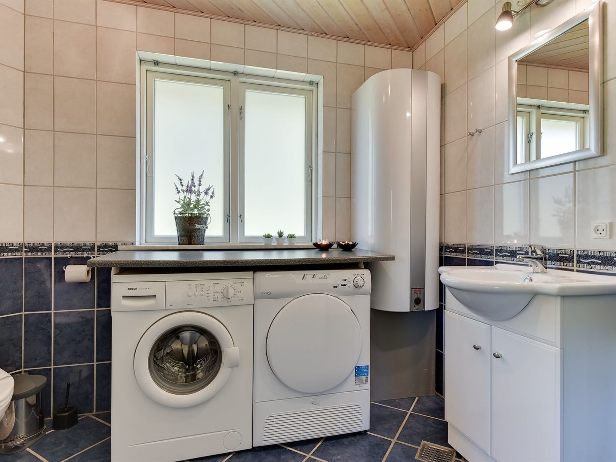 A modern bathroom with a Bosch washing machine, a sink, and a window with a potted plant.