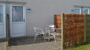 A building with numbered doors, a small outdoor seating area with metal chairs and a table, and a wooden fence. - "Tatianna" - 500m from the sea by Interhome (Rømø)