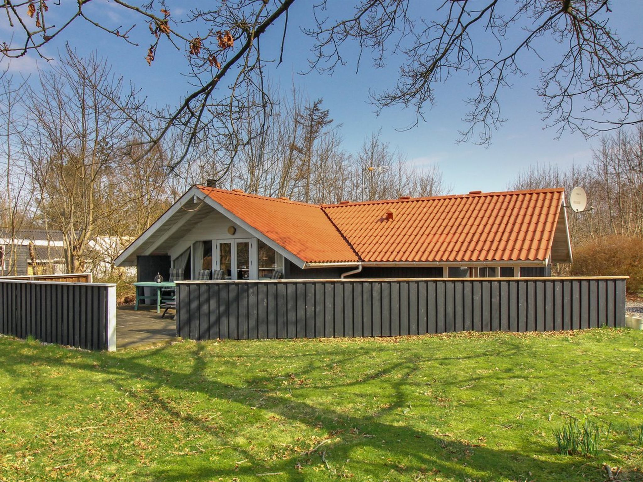Una casa a un piano con tetto rosso spiovente, un cortile recintato e cielo sereno.