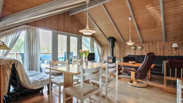 A spacious loft-style room with a high ceiling, wooden beams, a dining area with a table and chairs, a sofa, and a fireplace.