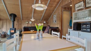 A cozy cabin interior with a wooden interior, a dining table with chairs, a sofa, a fireplace, and a shelf with glassware. - "Carlotta" - 12km from the sea by Interhome (Oksbøl)