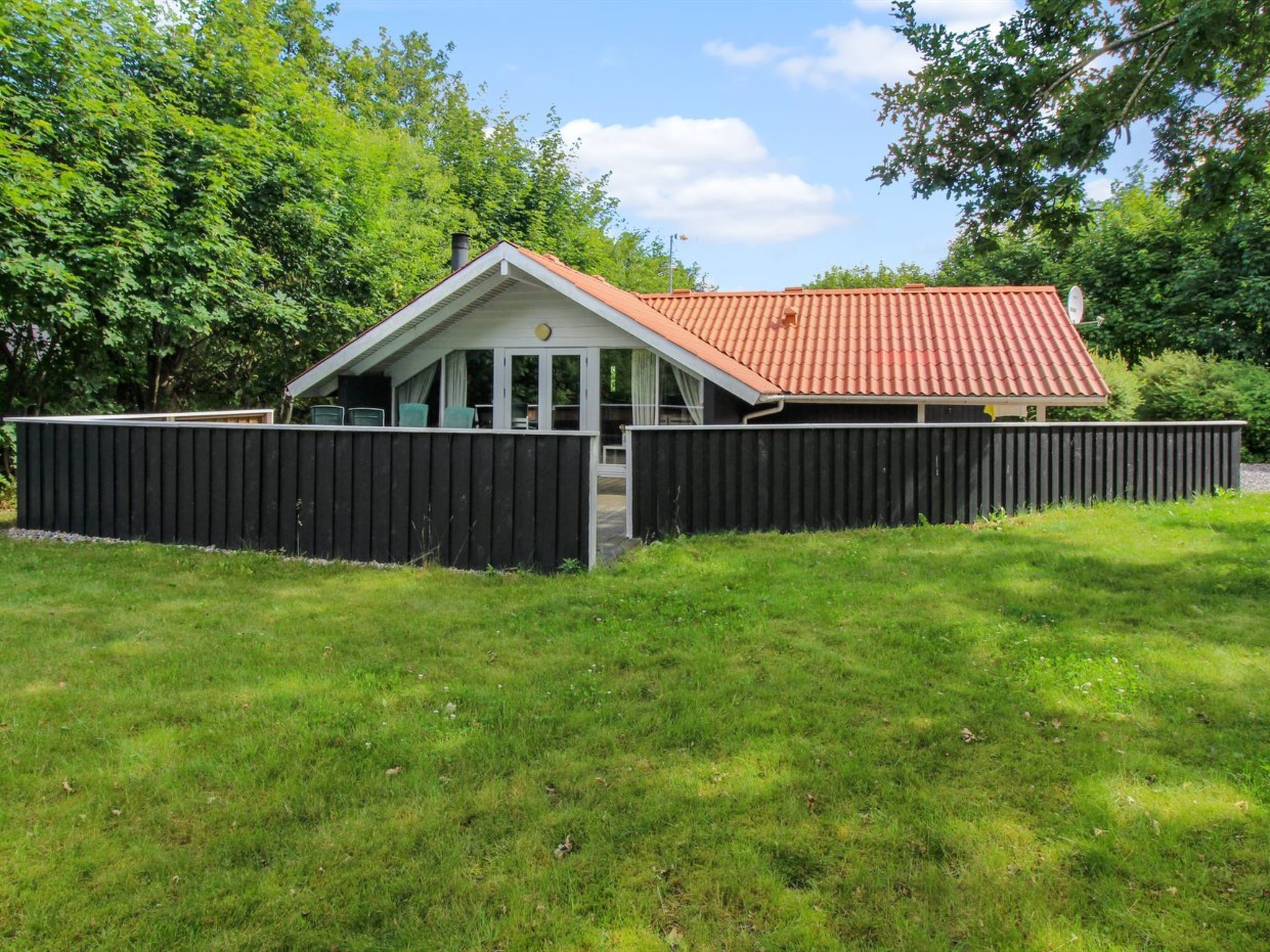 Ein Haus mit rotem Ziegeldach, schwarzem Zaun und einem Rasen.