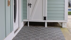 A covered porch with a metal grate entrance, a white door with a diagonal design, and a black lantern on the wall.
