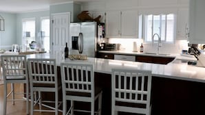A modern kitchen with white cabinetry, a large island with bar stools, and a stainless steel refrigerator.