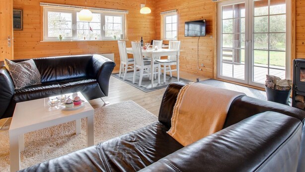 Ein gemütliches Blockhaus-Interieur mit einer schwarzen Ledersofa, einem Esstisch mit Stühlen, einem Kamin und großen Fenstern.