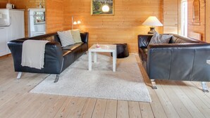 Ein gemütliches Blockhaus-Interieur mit zwei schwarzen Ledersofas, einem weißen Couchtisch und einer Holzbalkendecke.