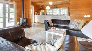 Ein gemütliches Blockhaus-Interieur mit Kamin, Ledersofas, Küchenbereich und großen Fenstern.