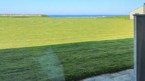 Een grasveld met een gebouw op de voorgrond en een helder uitzicht op de oceaan op de achtergrond.