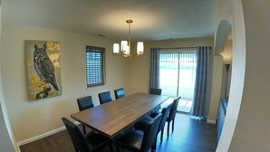 A dining room with a long wooden table, six chairs, a chandelier, and a painting of an owl on the wall. - Lakefront living on the 4MM - Best views on the Lake! (Rocky Mount)