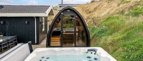A hot tub in a garden with a view of a house and a hill.