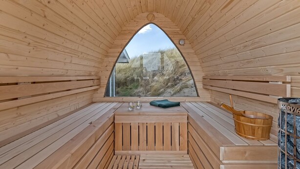 Eine Holzsauna mit Sitzbank, Eimer und Blick ins Freie.