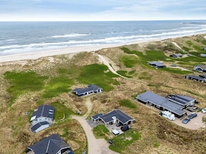 Vista aérea de una propiedad costera con varios edificios, una playa y un paisaje de dunas.